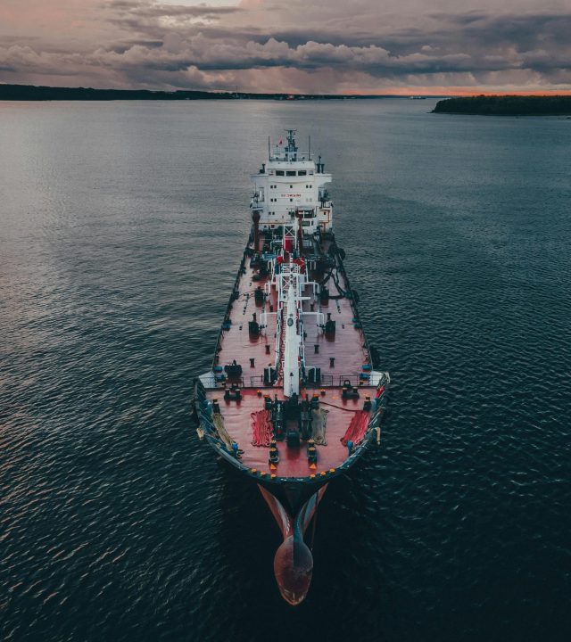 Aerial shot of a cargo ship navigating the calm ocean waters under twilight skies.